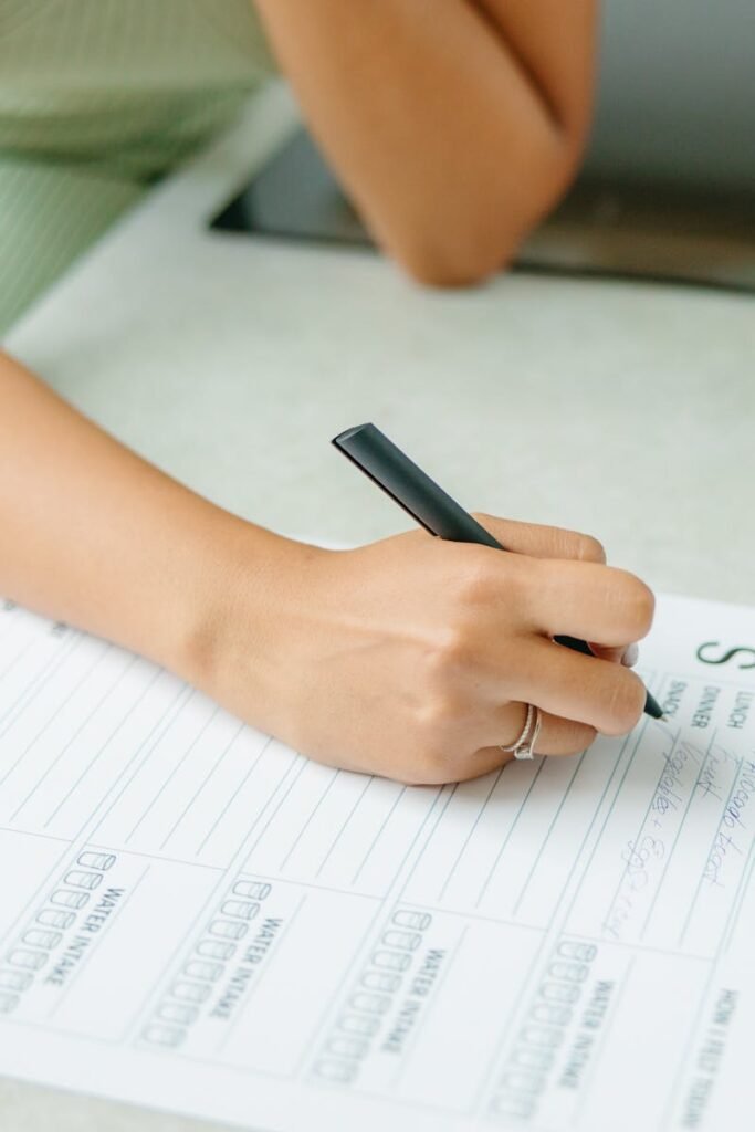 Close-up of a woman writing a weekly meal plan at home, promoting a healthy lifestyle.